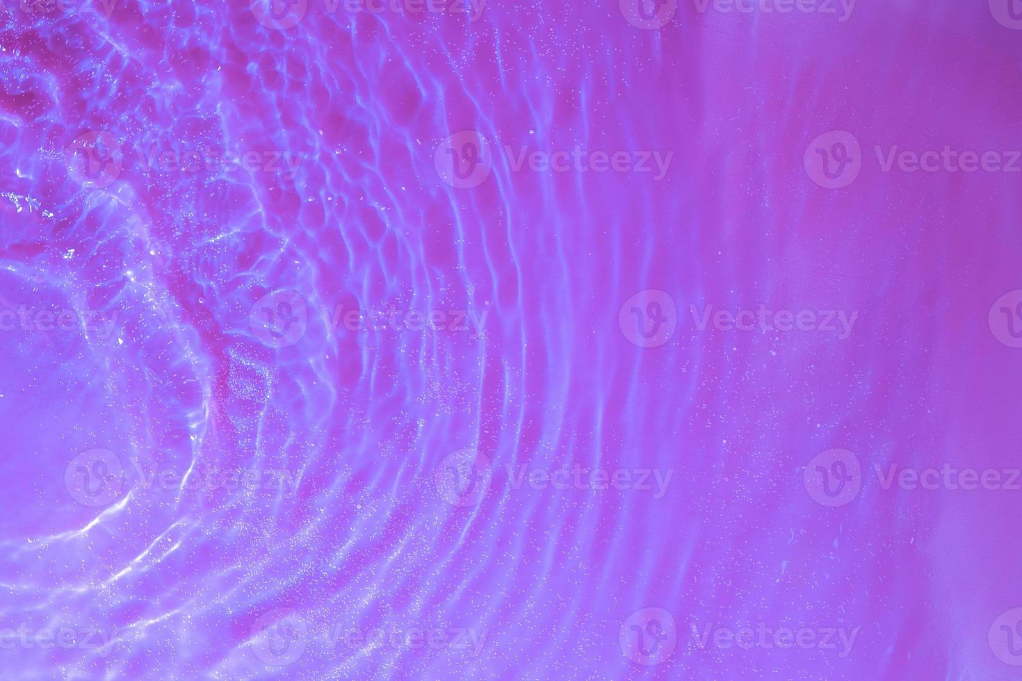 vatten stänk och vågor ovanifrån med bubblor i neonljus. vattenytans struktur foto