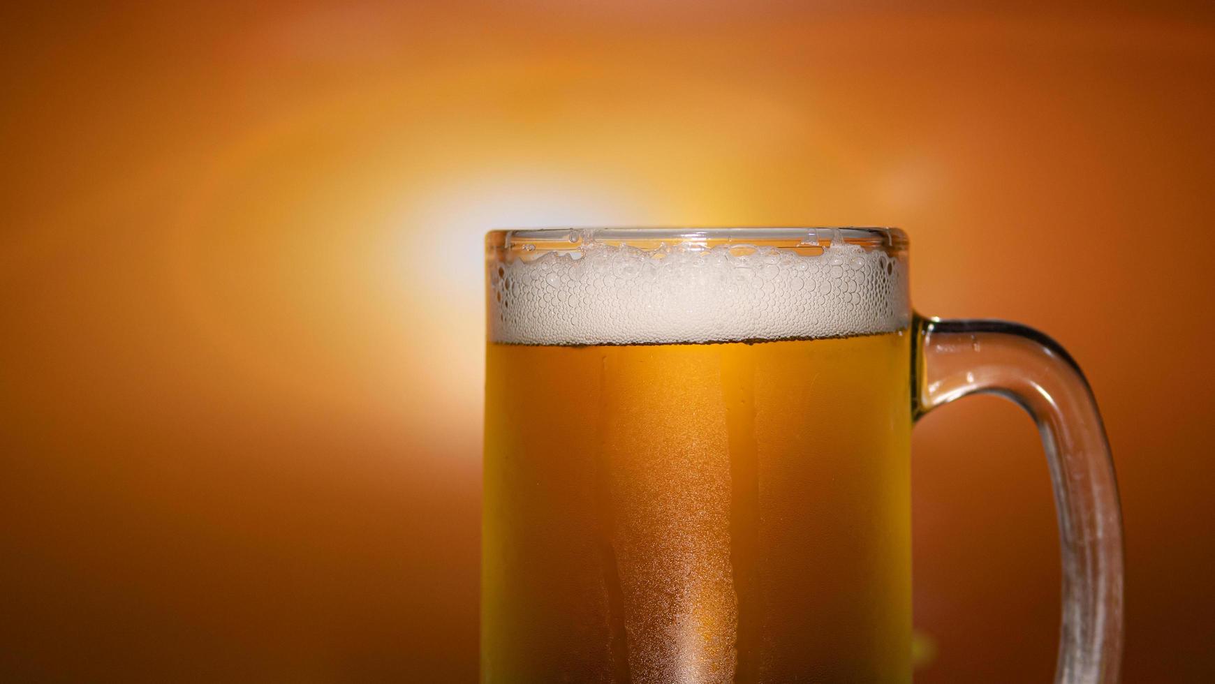häll upp ölen i ett klart glas med ölskum och bubbel. gyllene orange ljus bakgrund. foto