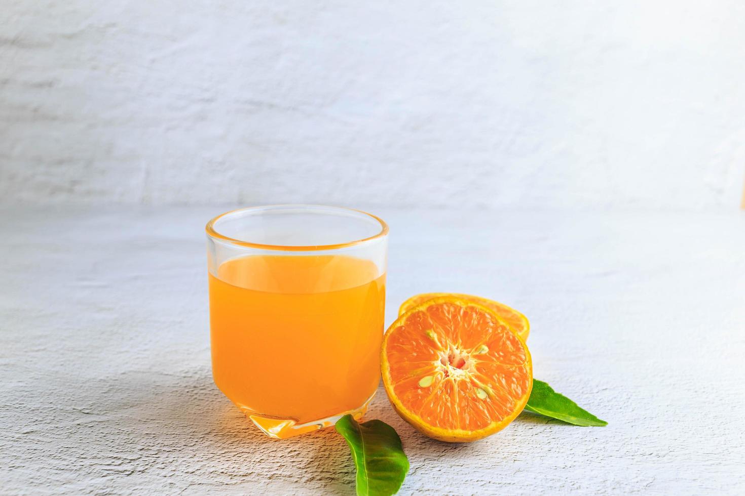 färskpressad apelsinjuice i ett glas och färska citrusfrukter på en vit bakgrund. foto