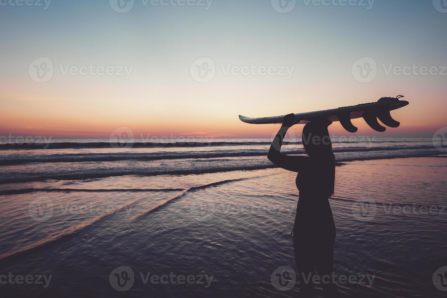 silhuett av vacker sexig surfer hona med surfbräda på sandstranden i solnedgången. vattensporter. surfing är en hälsosam aktiv livsstil. sommarlov. retro färgeffekt. foto