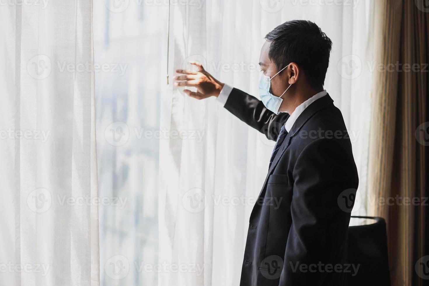 affärsman i medicinsk mask tittar ut genom fönstret foto