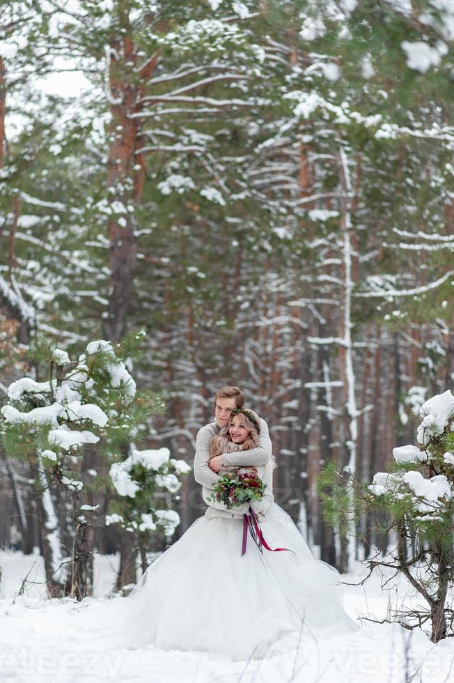 brudparet i beige stickade tröjor i snöig skog. nygifta rör vid pannan. vinterbröllop. kopieringsutrymme foto