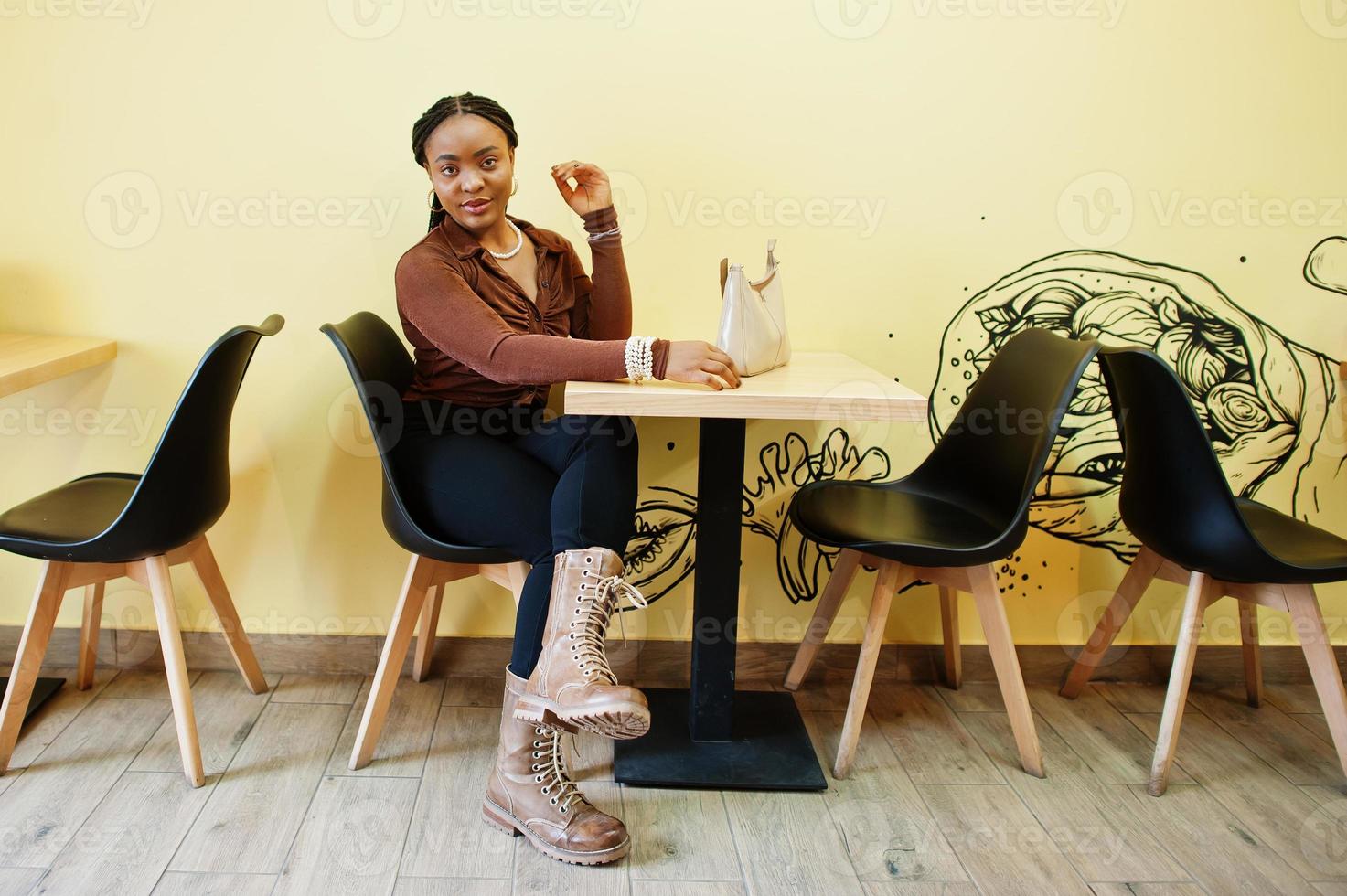 afrikansk amerikansk kvinna i brun skjorta och svarta byxor sitter på café. foto