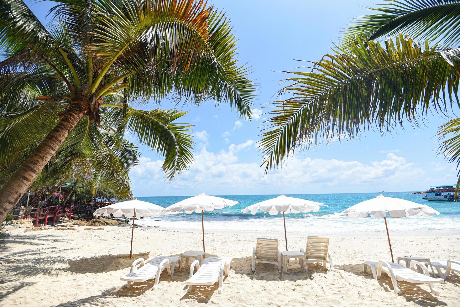 sommarlov naturresor vackert sommarlandskap med stol parasoll på sand - tropisk semester kokosnötsblad palmträd på stranden med solljus på blå himmel hav och hav bakgrund foto