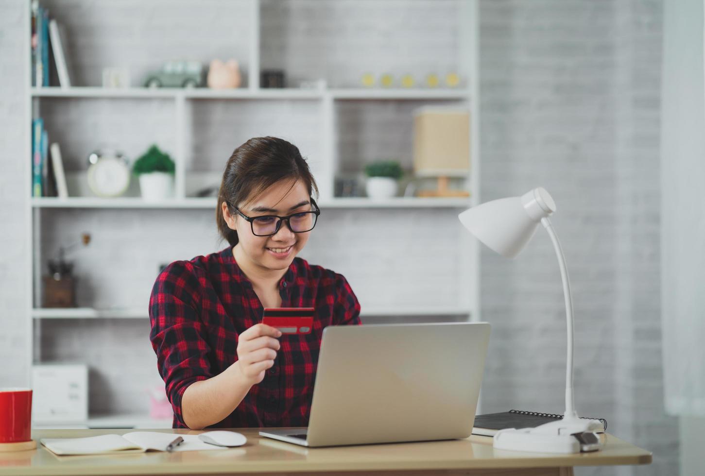 asiatiska frilanskvinnor använder laptop och rött kreditkort för att handla online på bordet. onlinebetalning online finansiella transaktioner. frilansarbete som säljer online. foto