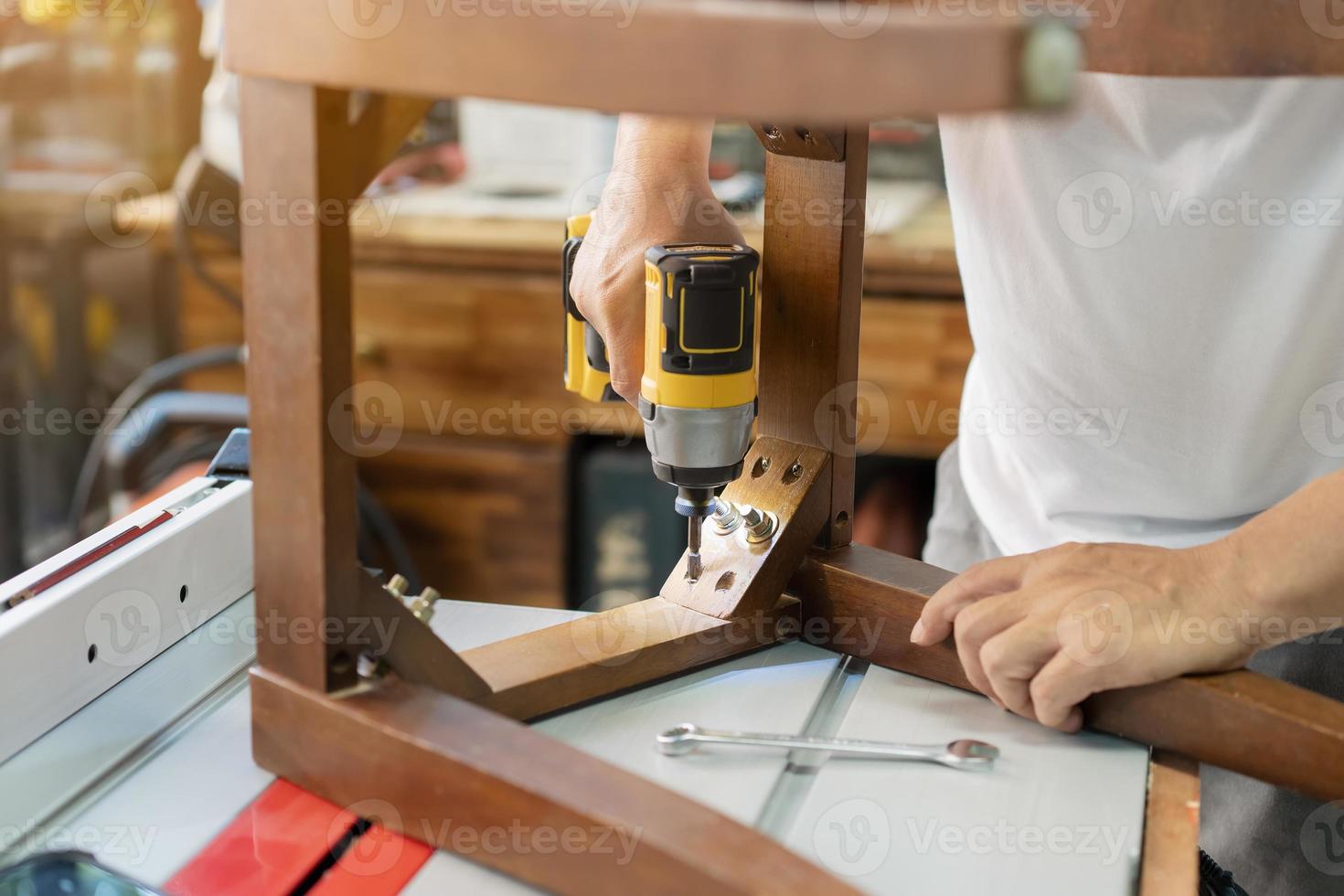 snickare reparation stol och använda elektrisk skruvmejsel på verkstad, möbel restaurering träbearbetning koncept. selektiv fokusering foto