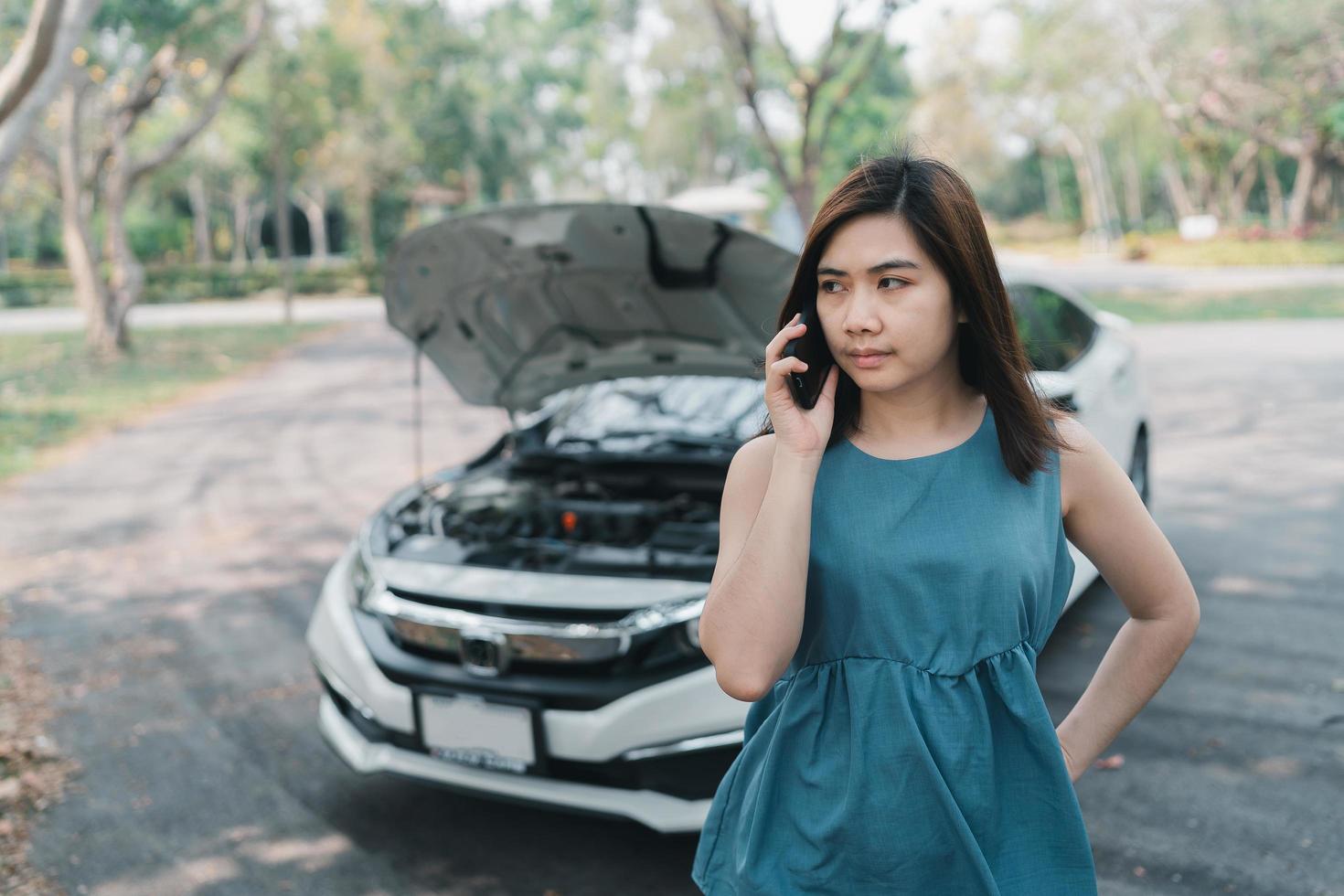 asiatisk kvinna ringer garage efter bil havererar. kvinna som öppnar huven och ringer till försäkringen eller någon som hjälper efter att bilen gått sönder, parkera på sidan av vägen. transport koncept. foto