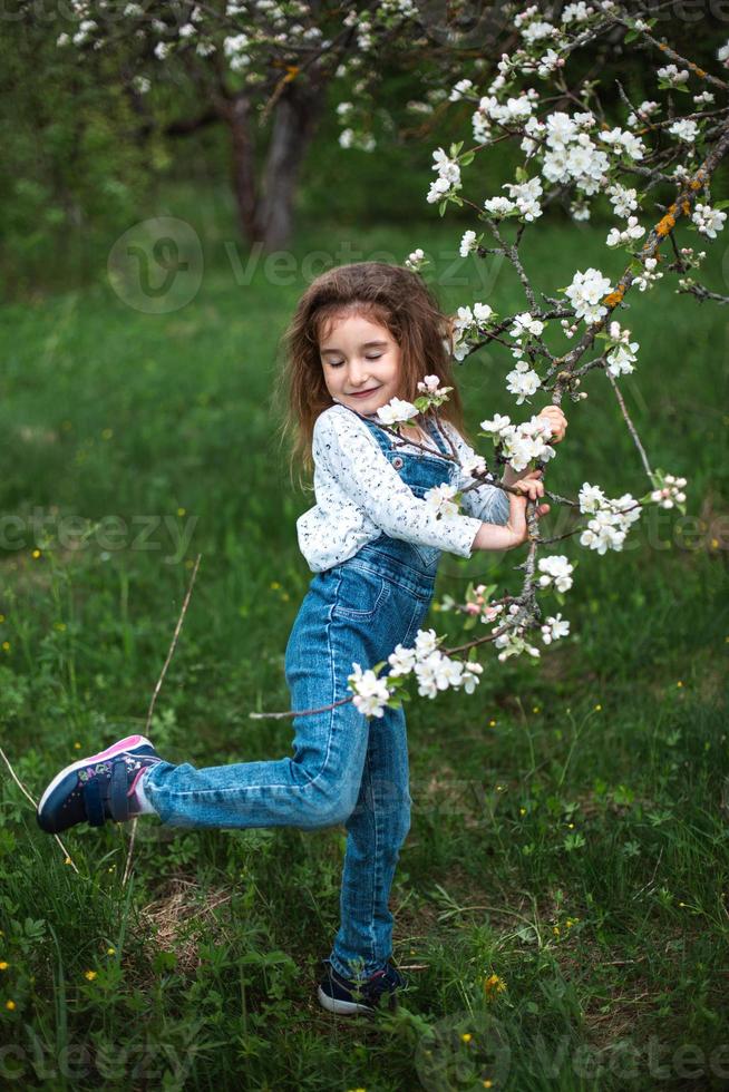 en söt liten flicka på 5 år i en blommande vit äppelodling på våren. vår, fruktträdgård, blomning, allergi, vårdoft, ömhet, omsorg om naturen. porträtt foto