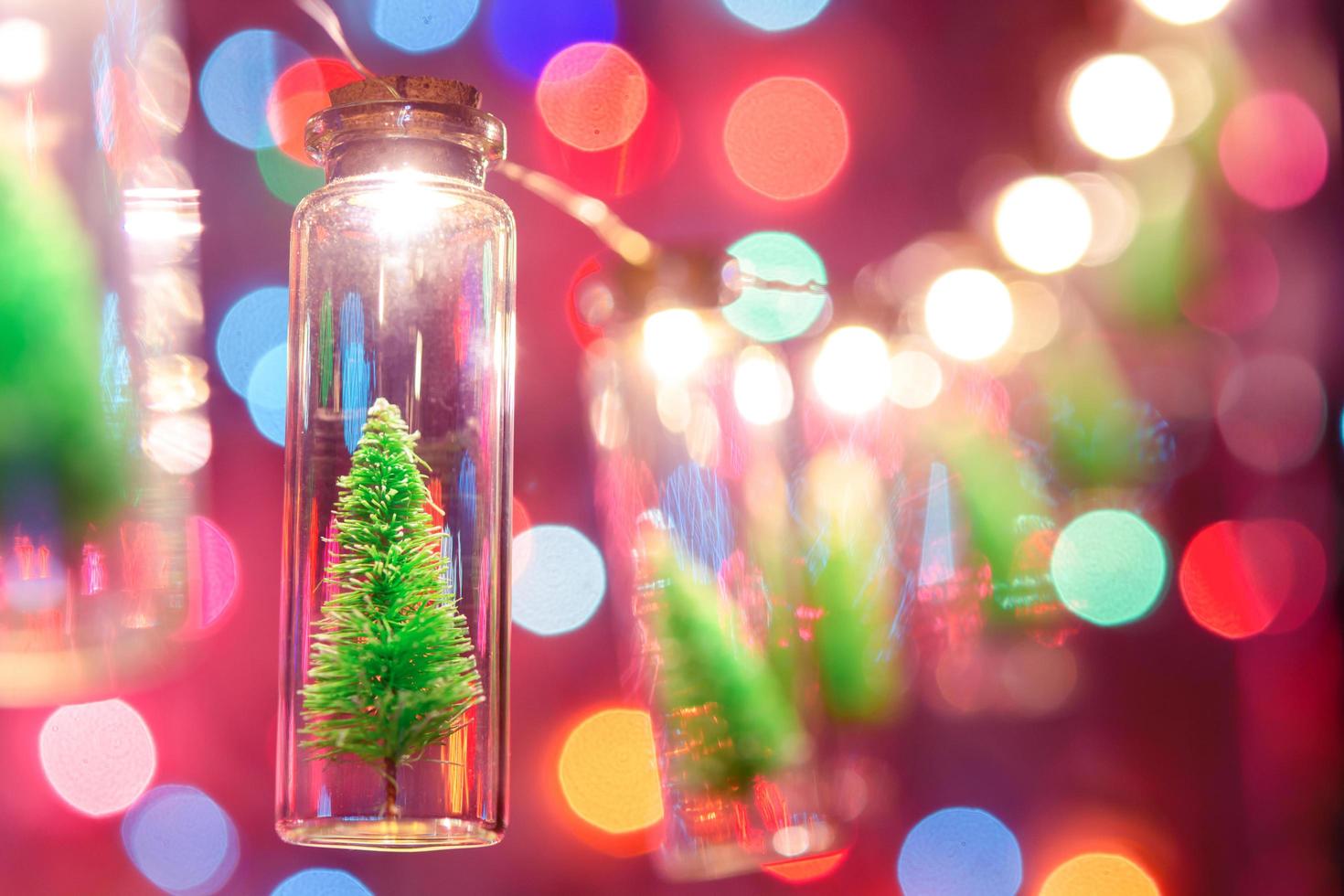 god Jul och Gott Nytt År. hängande liten julgran i glasburk på tallgrenar julgransgirland och ornament över abstrakt bokeh foto