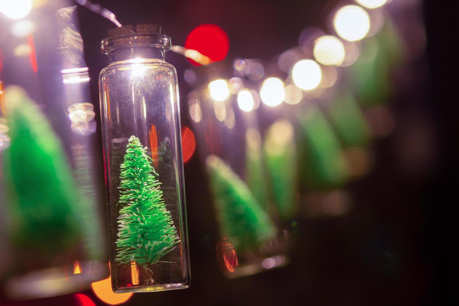 god Jul och Gott Nytt År. hängande liten julgran i glasburk på tallgrenar julgransgirland och ornament över abstrakt bokeh foto