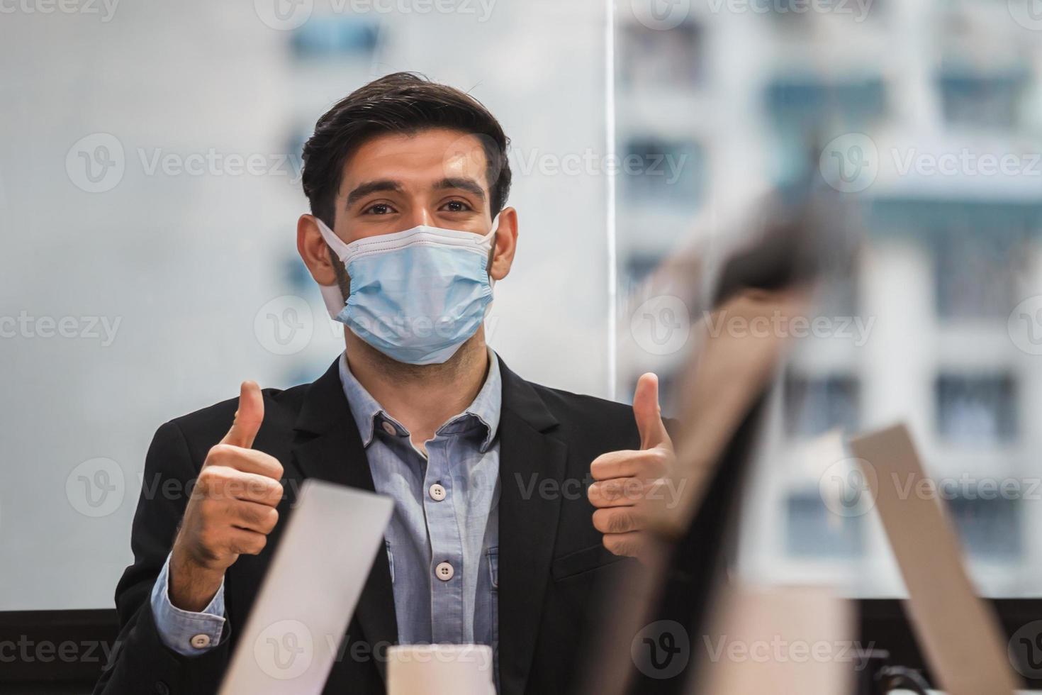unga affärsmän bär ansiktsmasker med tummen upp som ett tecken på framgång foto