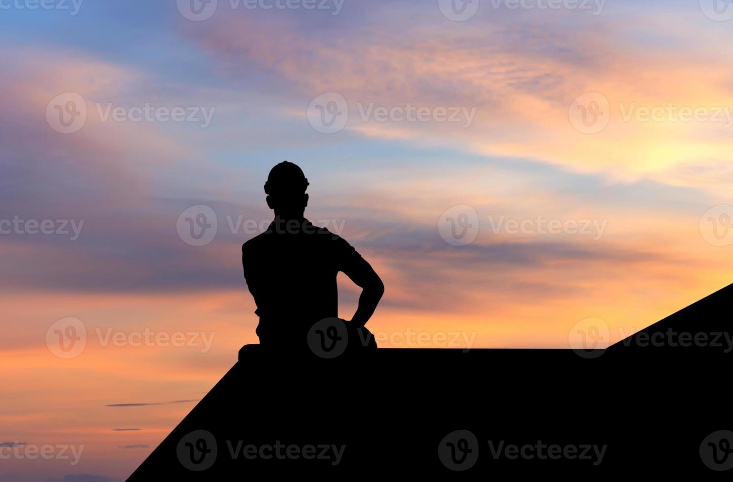 siluett av förmannen i hjälm sitter på containerlåda med solnedgångshimlen foto