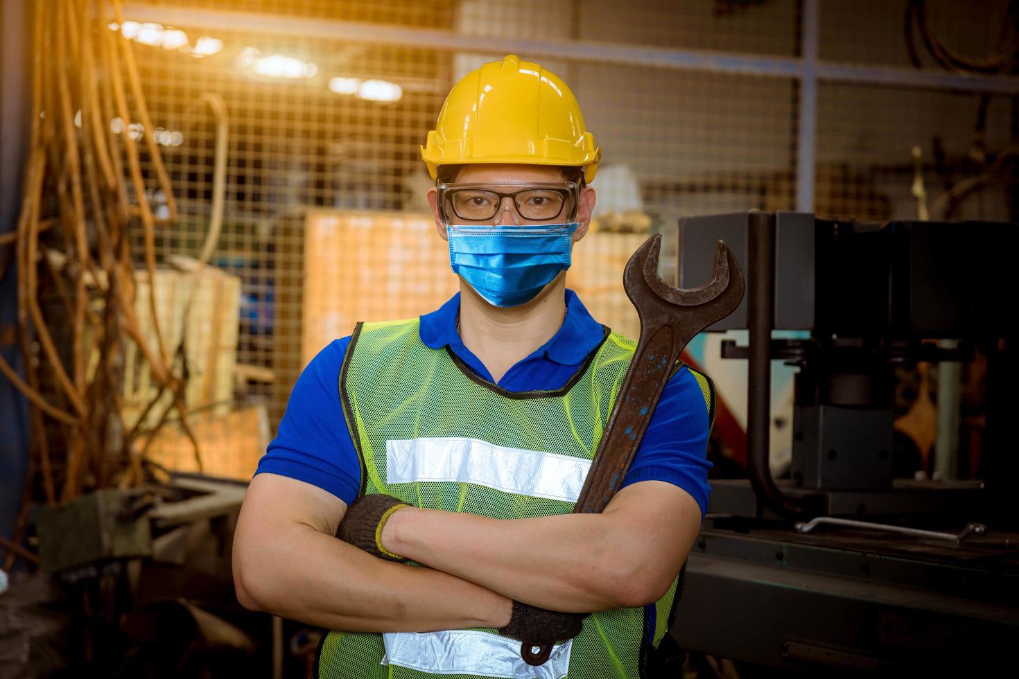 ingenjör under inspektion och kontroll av produktionsprocess på fabriksstation som håller en skruvmejsel genom att bära säkerhetsmask för att skydda mot föroreningar och virus i fabriken. foto