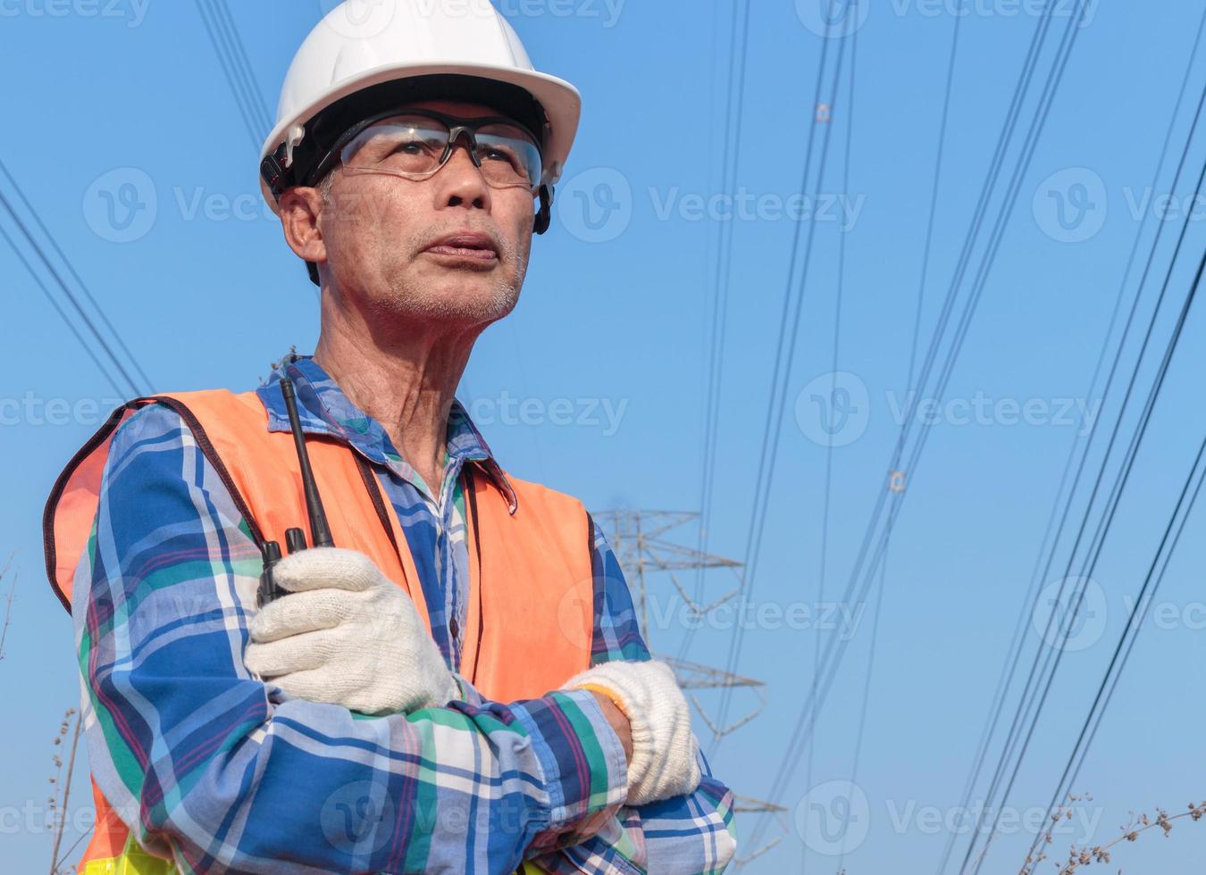 lågvinkelporträtt av en senior asiatisk elektriker som bär en hjälm och skyddsglasögon som håller en radiosändare. foto