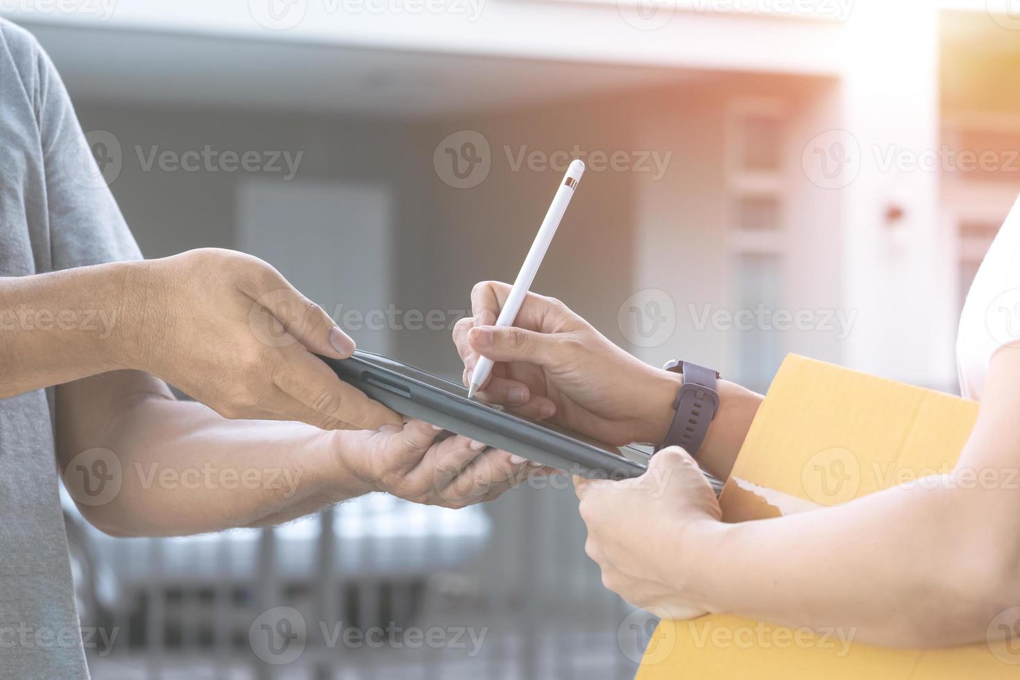 närbild kvinnlig hand med elektronisk penna för att underteckna signatur på surfplatta efter mottagen paketlåda från leveransmannen framför hemmet foto