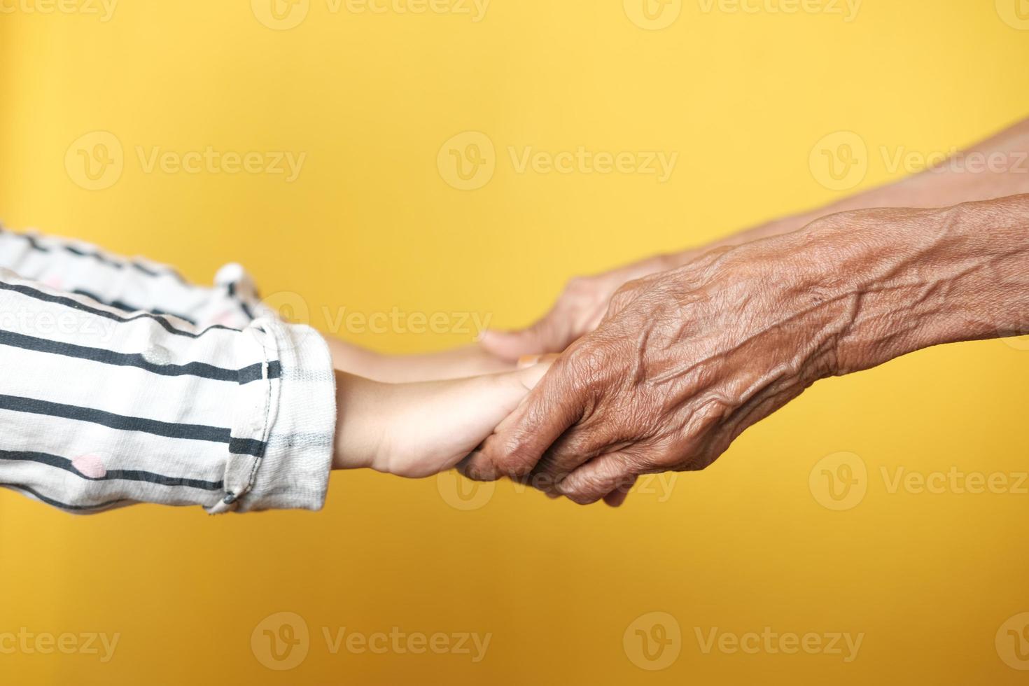 närbild av barn hand som håller senior kvinnors hand mot gul bakgrund foto