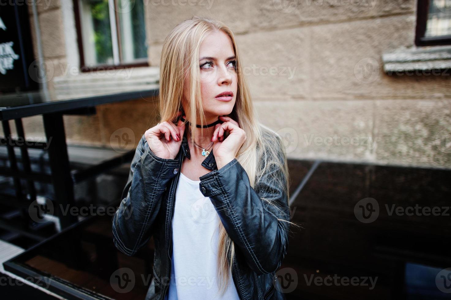 snygg blond kvinna bär på jeans, choker och skinnjacka på gatan. mode urban modell porträtt. foto