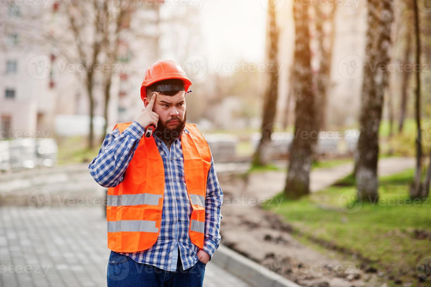 porträtt av brutala skäggarbetare man kostym byggnadsarbetare i säkerhetsorange hjälm mot trottoartänkande. foto