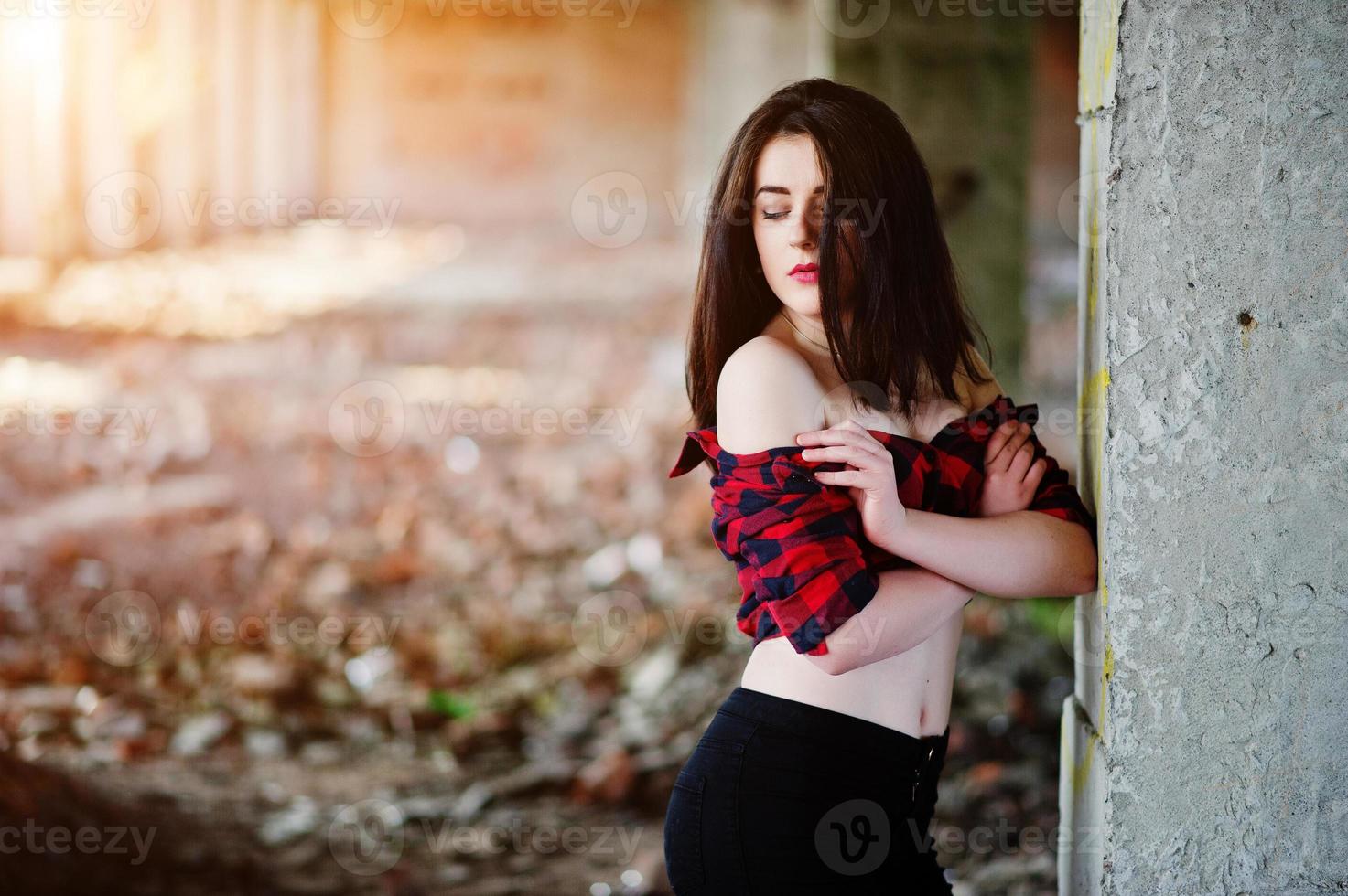 porträtt flicka med röda läppar bär en röd rutig skjorta med bara axlar poserade sexig bakgrund övergiven plats. foto