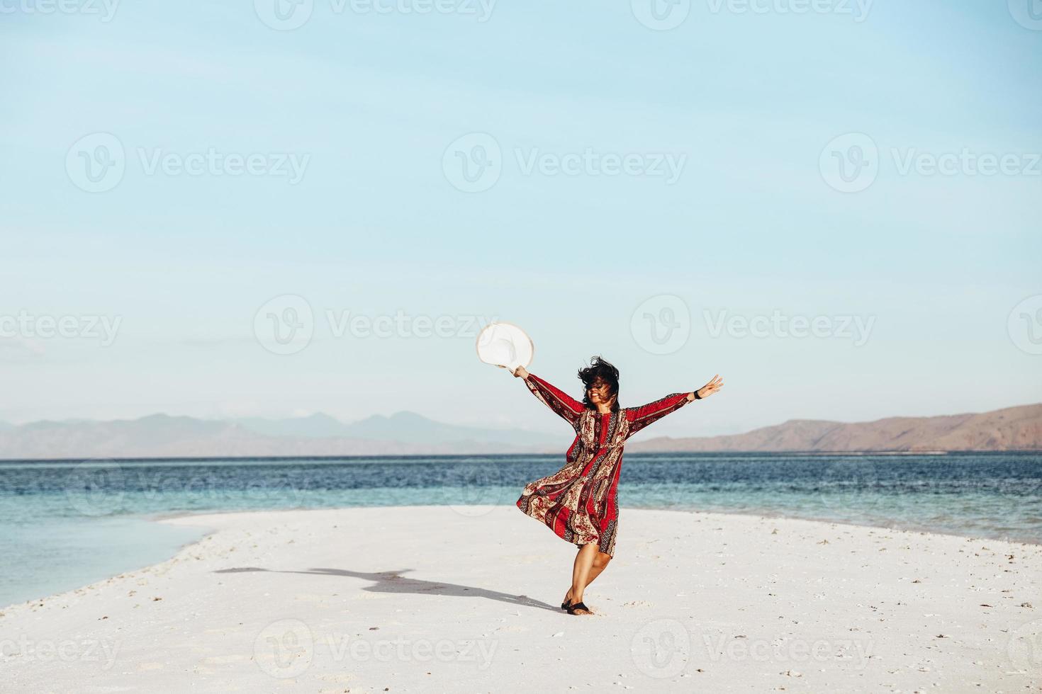 glad asiatisk tjej dansar på vit sandstrand omgiven av havet foto