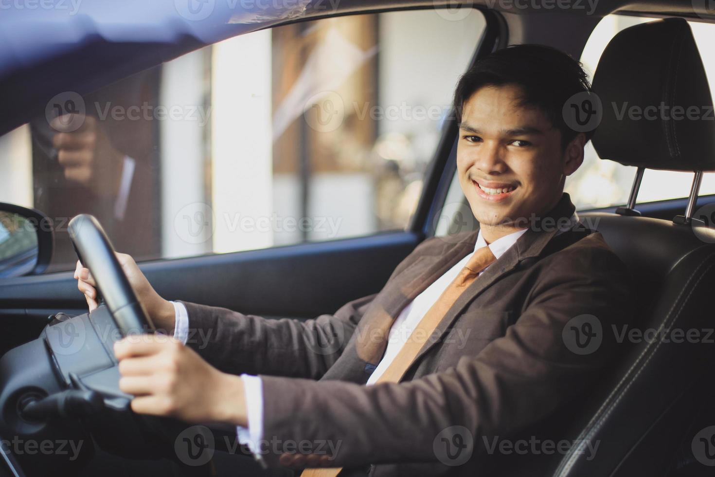 asiatisk affärsman kör bil medan han ler mot kameran foto