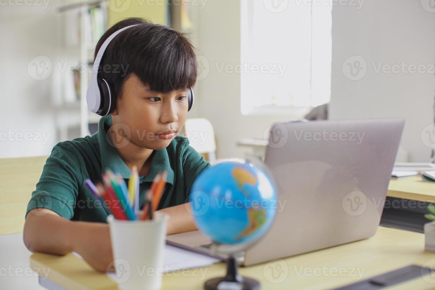 asiatisk student i hörlurar skriver på papper medan du tittar på en bärbar dator foto