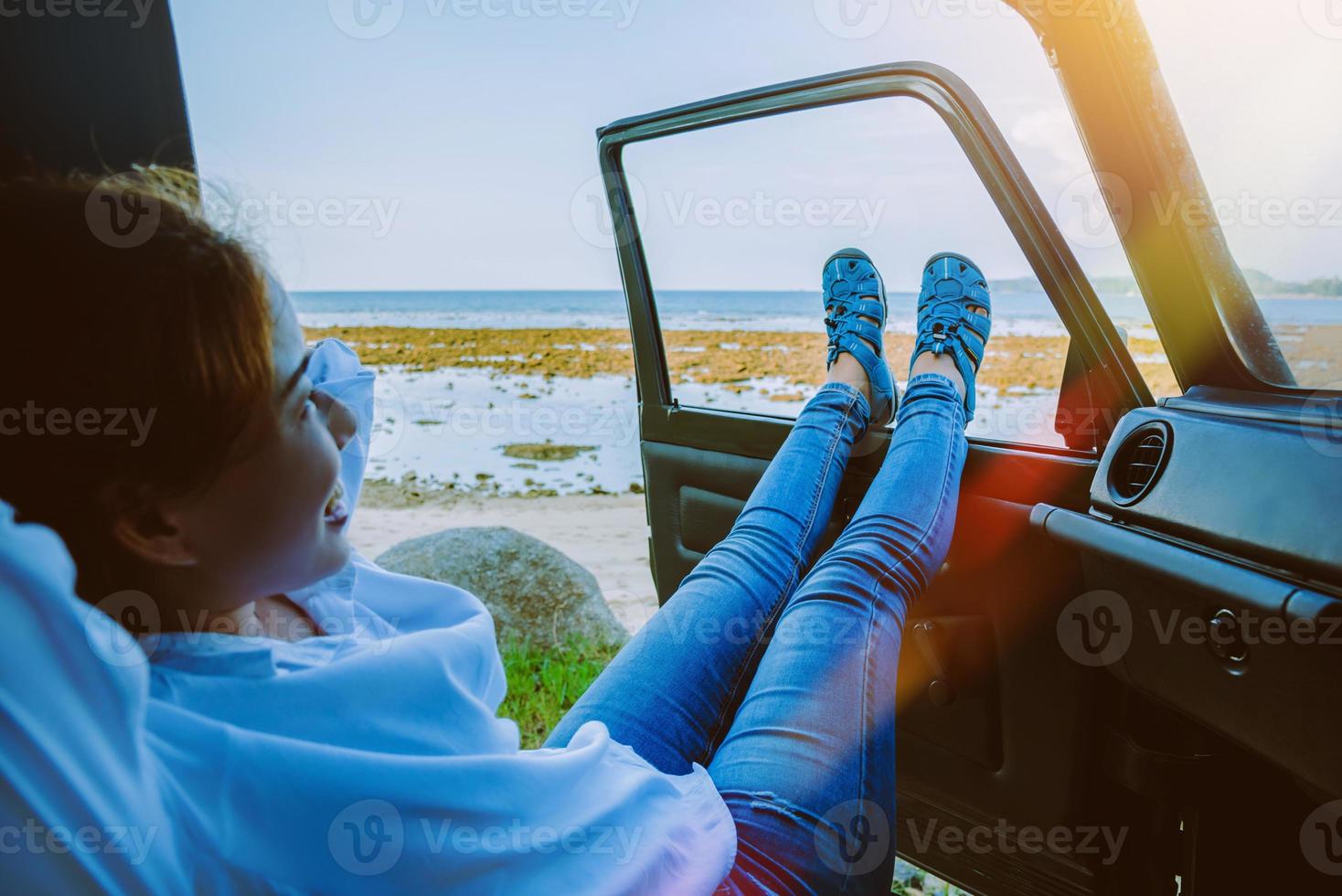 asiatisk kvinna reser naturen. resa koppla av på stranden på sommaren. sitter i bilen glad över att se havet och benet utanför bilen. foto