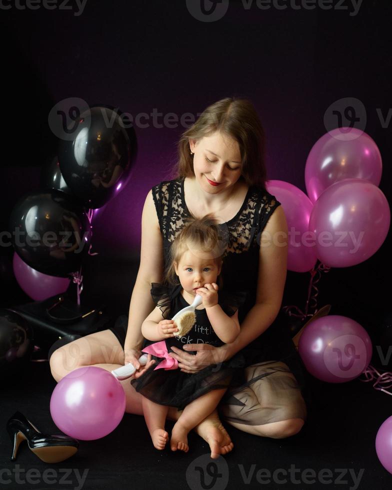 första året flickans födelsedagsfest dag. ballonger och semester inomhus. barnets födelsedag. liten söt flicka med sin mamma i svart klänning foto