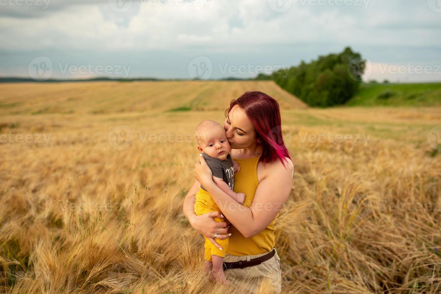 en mamma håller ömt sin tre månader gamla son i famnen på ett vetefält. foto