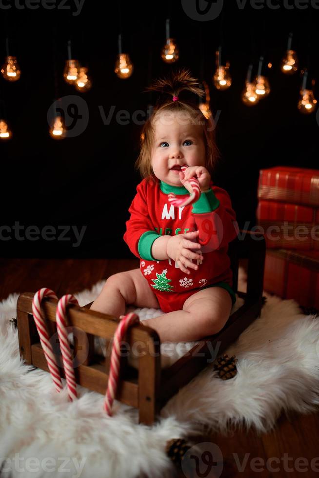 7 månader gammal flicka i en röd juldräkt på en bakgrund av retro girlander sitter på en päls foto