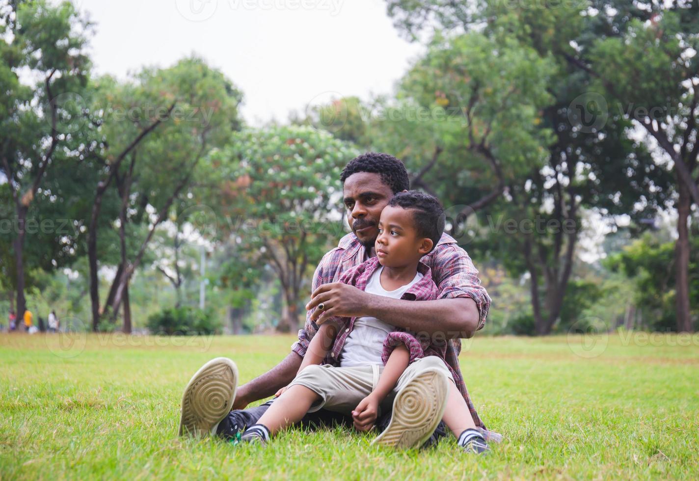 glad afrikansk amerikansk far medan han kramar och bär sin son, pappa kysste sin son i parken, glada svarta familjekoncept foto