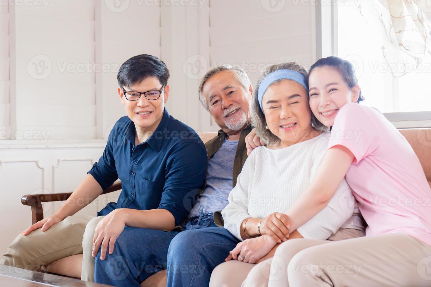 glad asiatisk familj i vardagsrummet, äldre far mamma och medelålders son och dotter sitter på soffan och tittar på kameran, lycka familj koncept foto