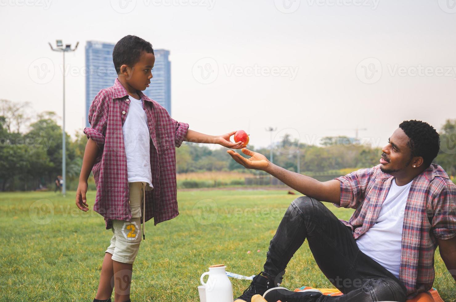 son ger rött äpple till sin far, afrikansk amerikansk pojke gav ett äpple till sin far, lycka familj i parkkoncept foto