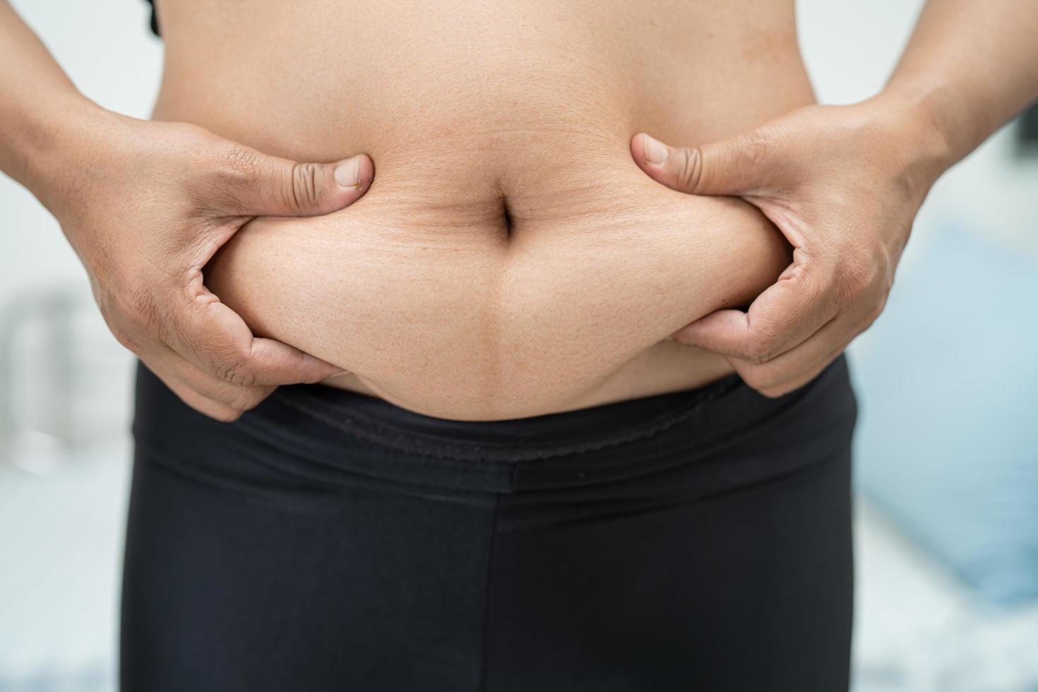 överviktig asiatisk kvinna visar fet mage på kontoret. foto