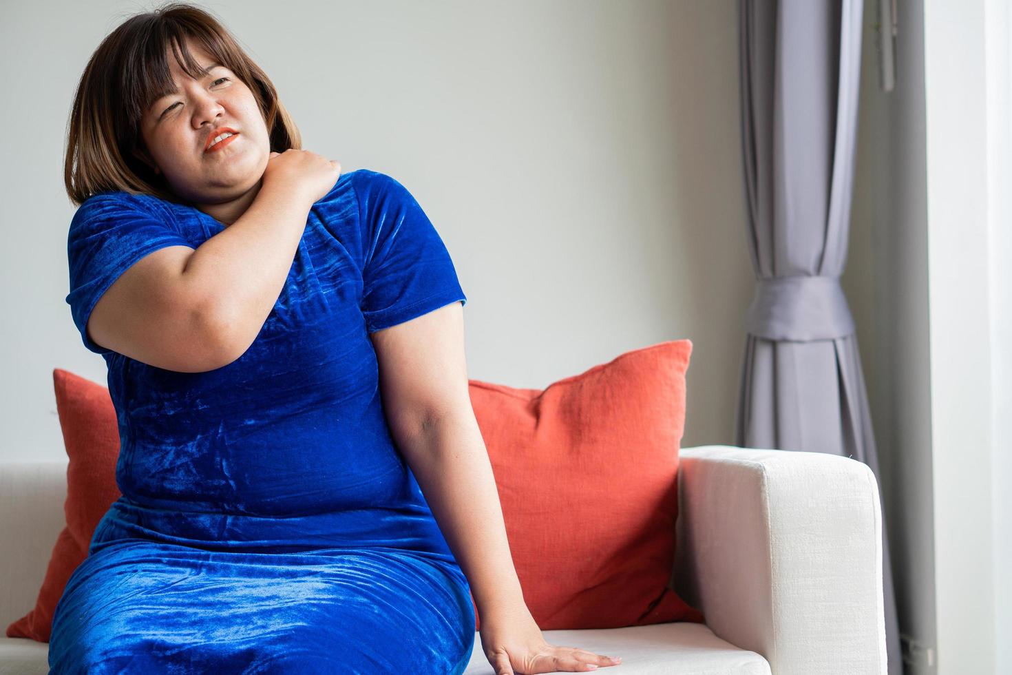 överviktiga asiatiska kvinnor sitter i soffan i vardagsrummet. och handtaget på axeln på grund av kontorssyndrom, sjukdom och hälsovårdskoncept. foto