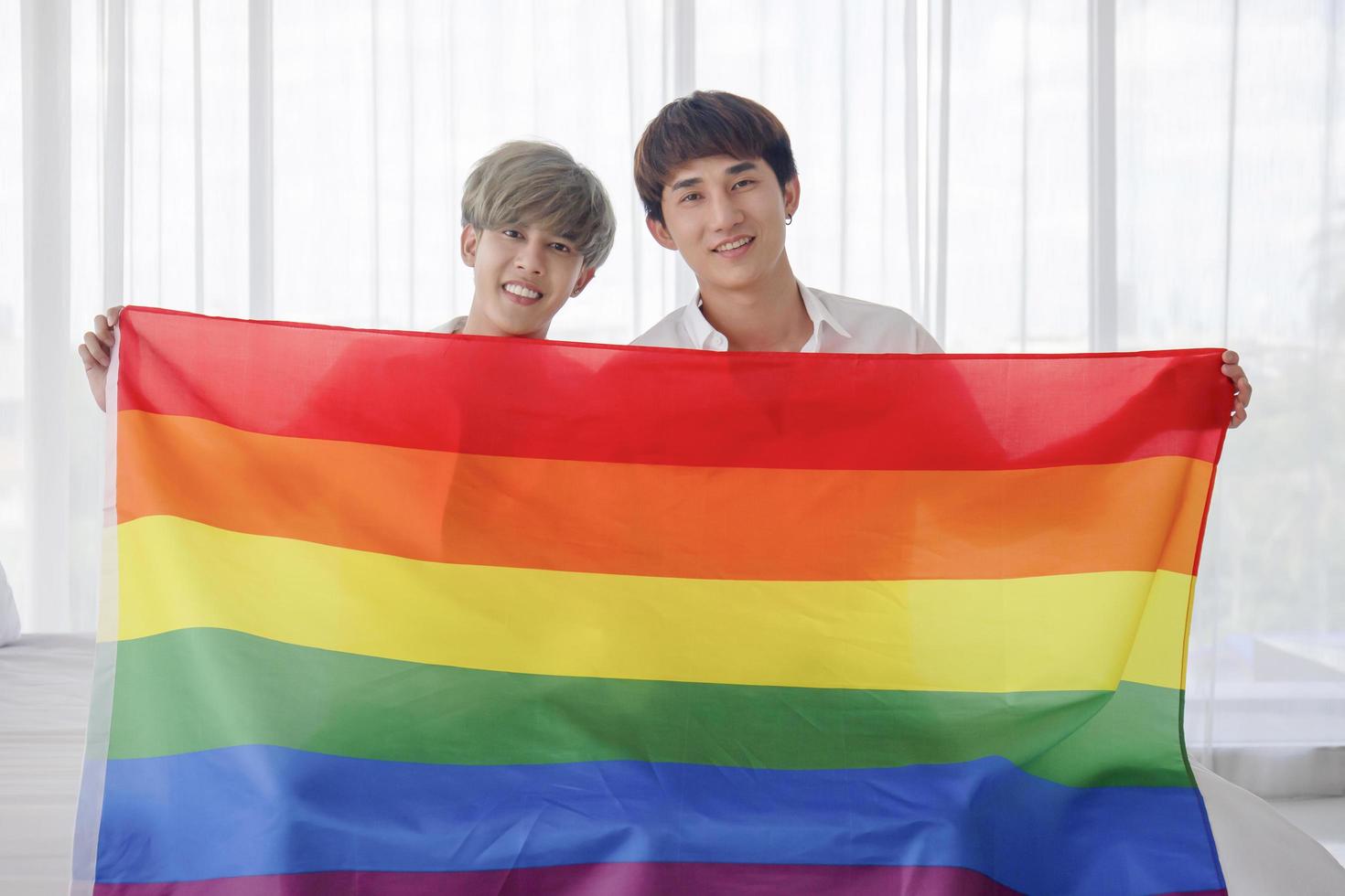manligt par med asiatisk man fångar flaggan som symboliserar könsmångfald och uttrycker öppet homosexuella män som accepterar hbt-koncept. foto