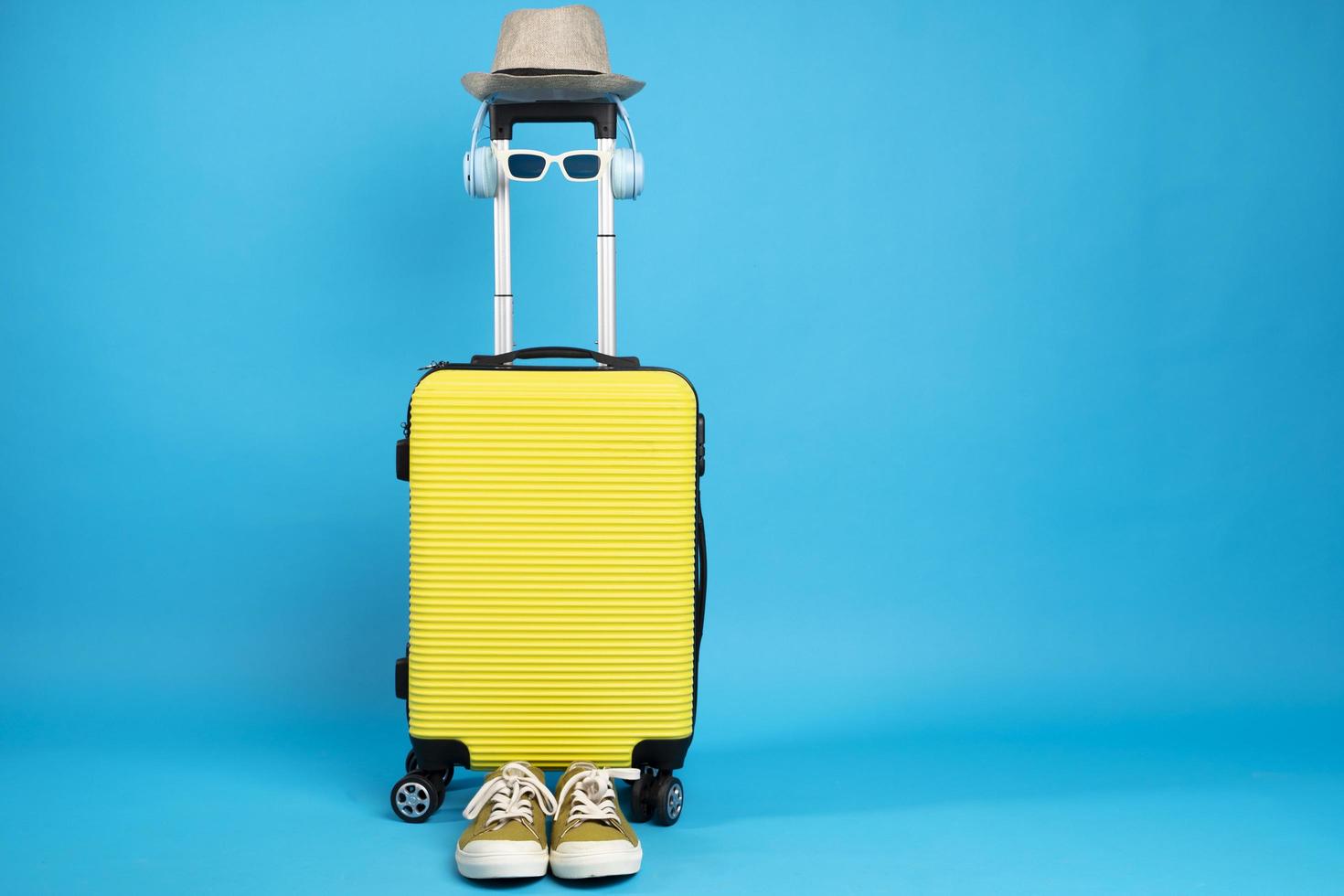 gul resväska med solglasögon, hatt och kamera på pastellblå bakgrund. resekoncept. minimal stil foto