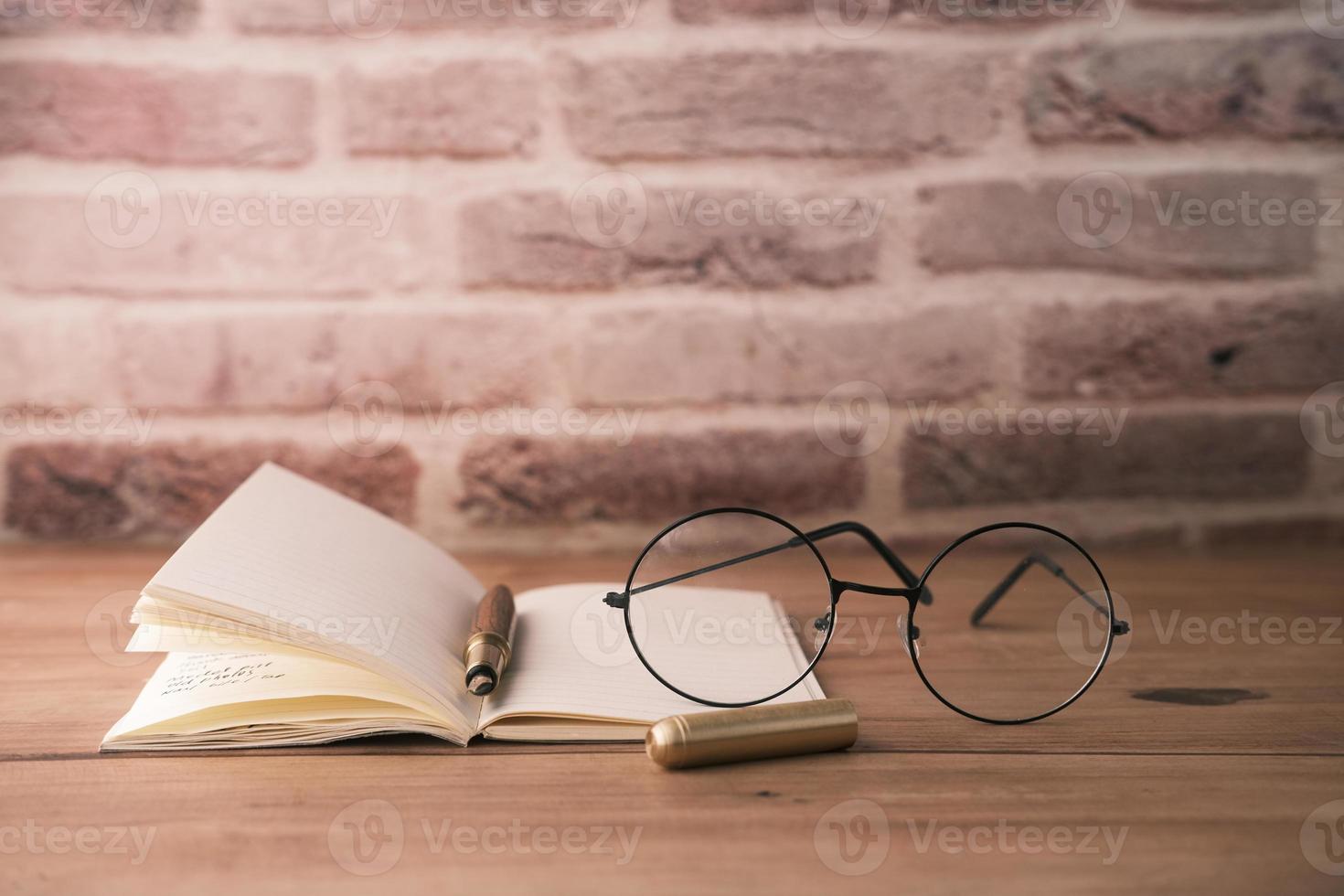 anteckningsblock, glasögon och en penna på träbord foto