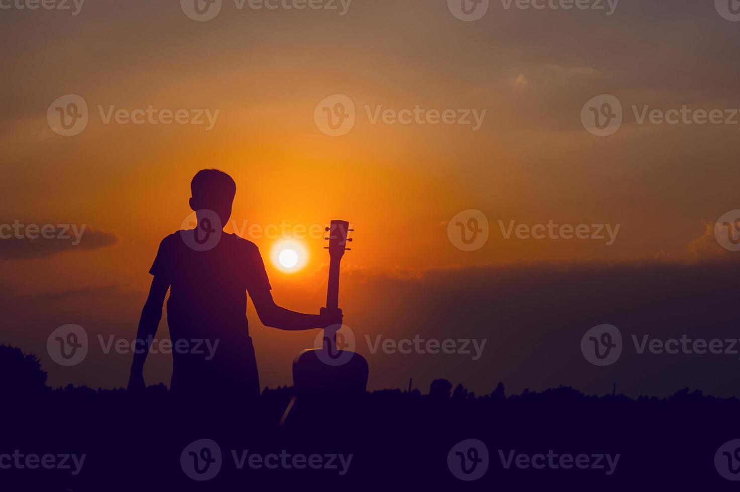 siluetten av en gitarrist som håller en gitarr och har ett solnedgångs-, siluettkoncept. foto