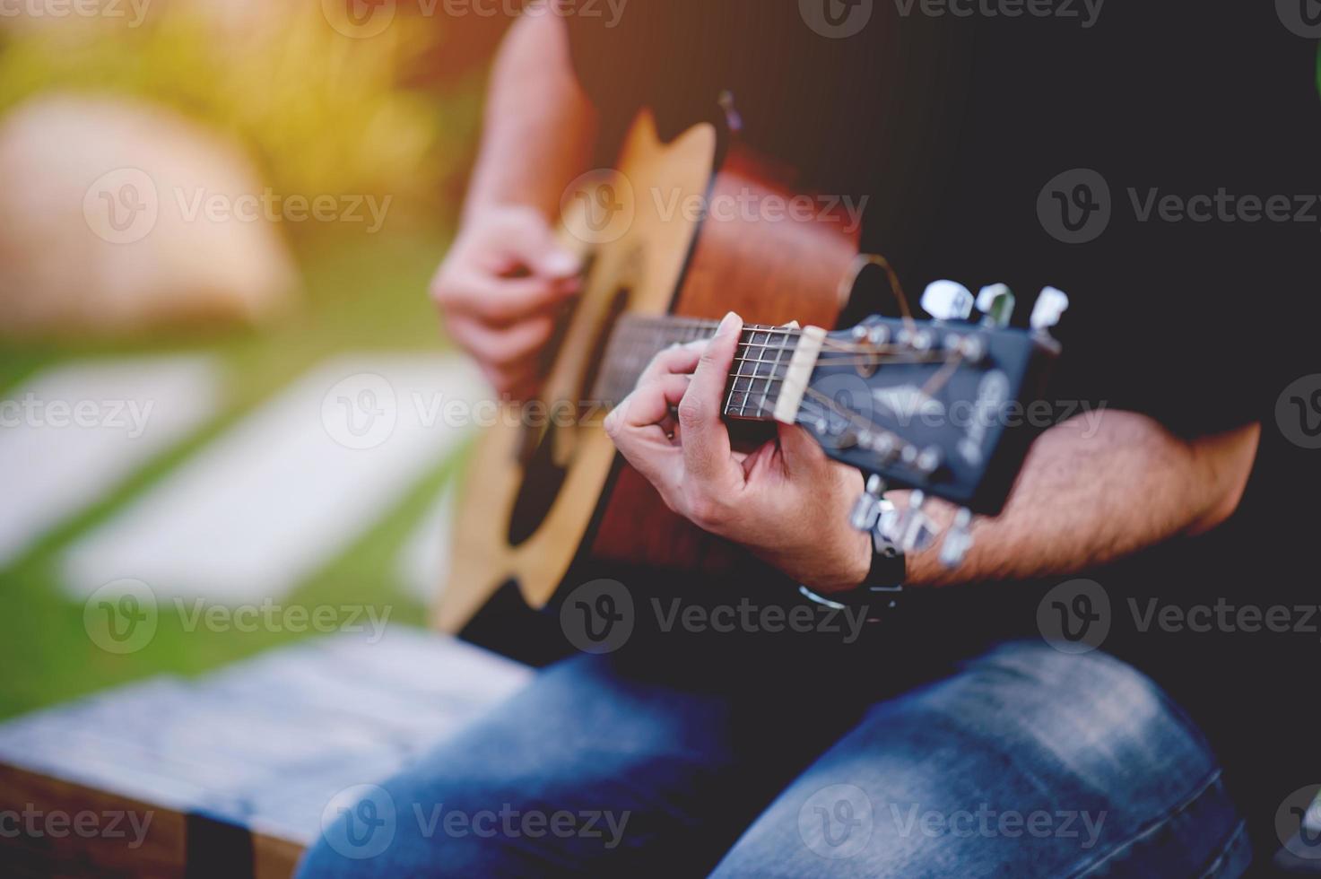 bild av en gitarrist, en ung man som spelar gitarr medan han sitter i en naturlig trädgård, musikkoncept foto