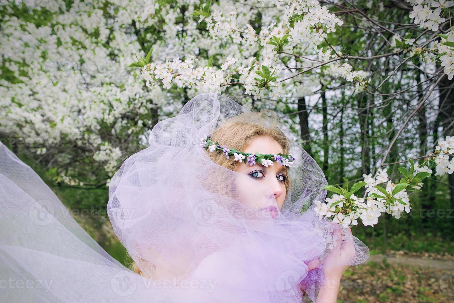 vacker ung blond kvinna i blomkrans blommande träd på våren foto