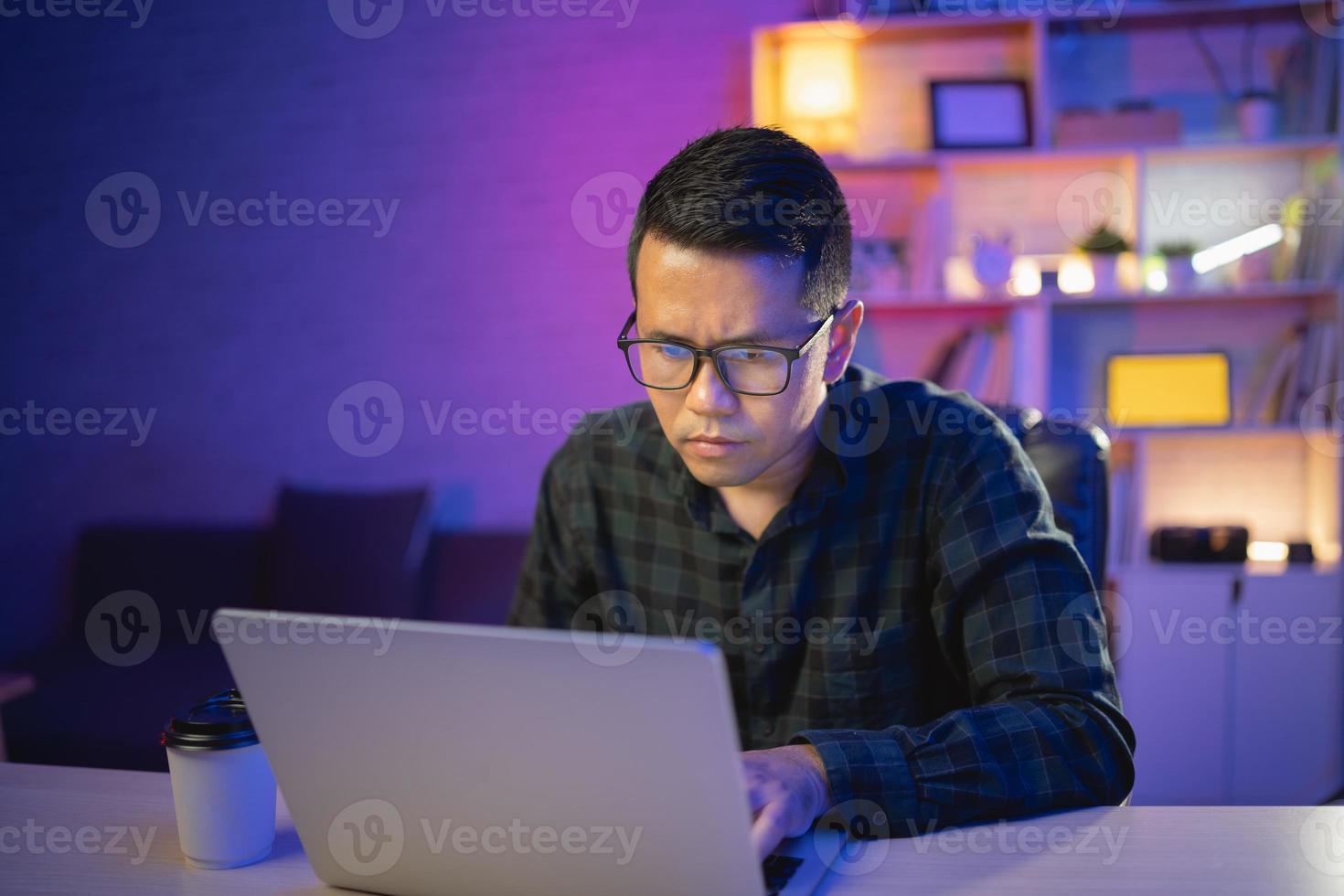 frilansande man som arbetar på laptop hemma på natten. man utvecklare programmerare, dataingenjör, tänkande, seriös medan du arbetar hemma på natten. frilansarbete och arbeta hemifrån koncept. foto