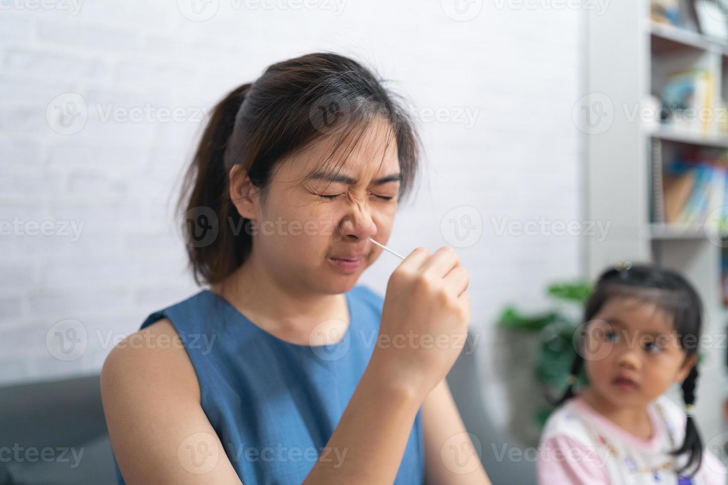 asiatisk kvinna hand som håller atk, antigen kit självtest och dotter tittar på sin mamma, näspinne test för eventuell infektion av coronavirus, covid-19 hemma. foto