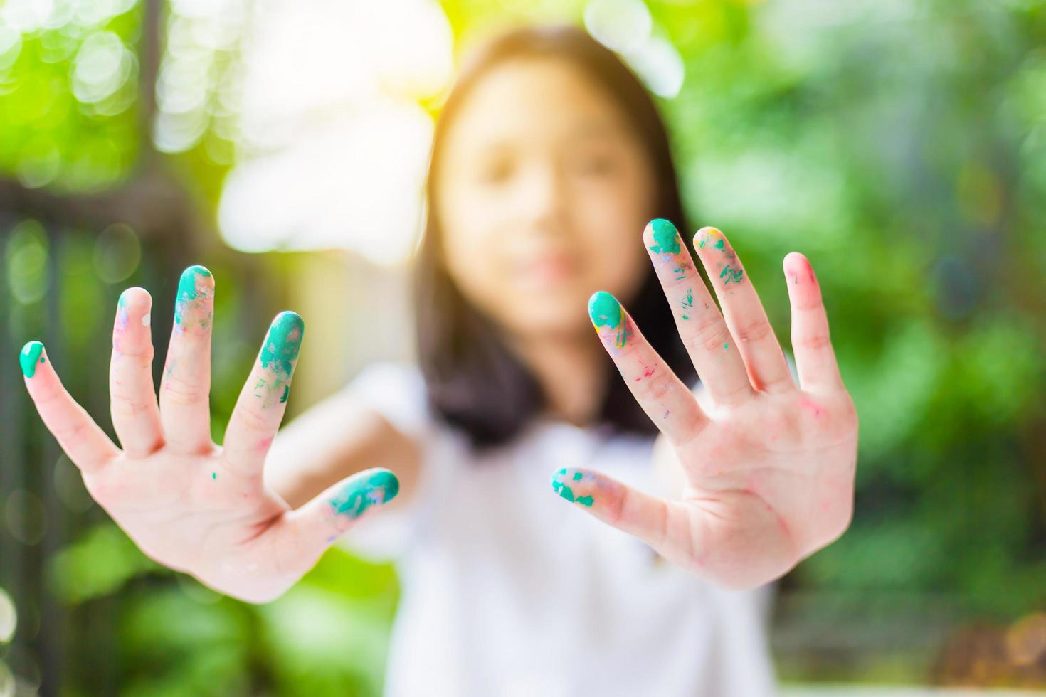 rolig barnflicka visar händerna smutsiga med färg, glad liten söt tjej som leker och lär sig med att färga färgerna foto