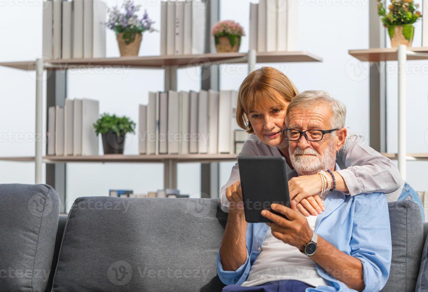 porträtt av lyckliga äldre par i vardagsrummet, äldre kvinna och en man som använder surfplatta-smartphone på mysig soffa hemma, lyckliga familjekoncept foto