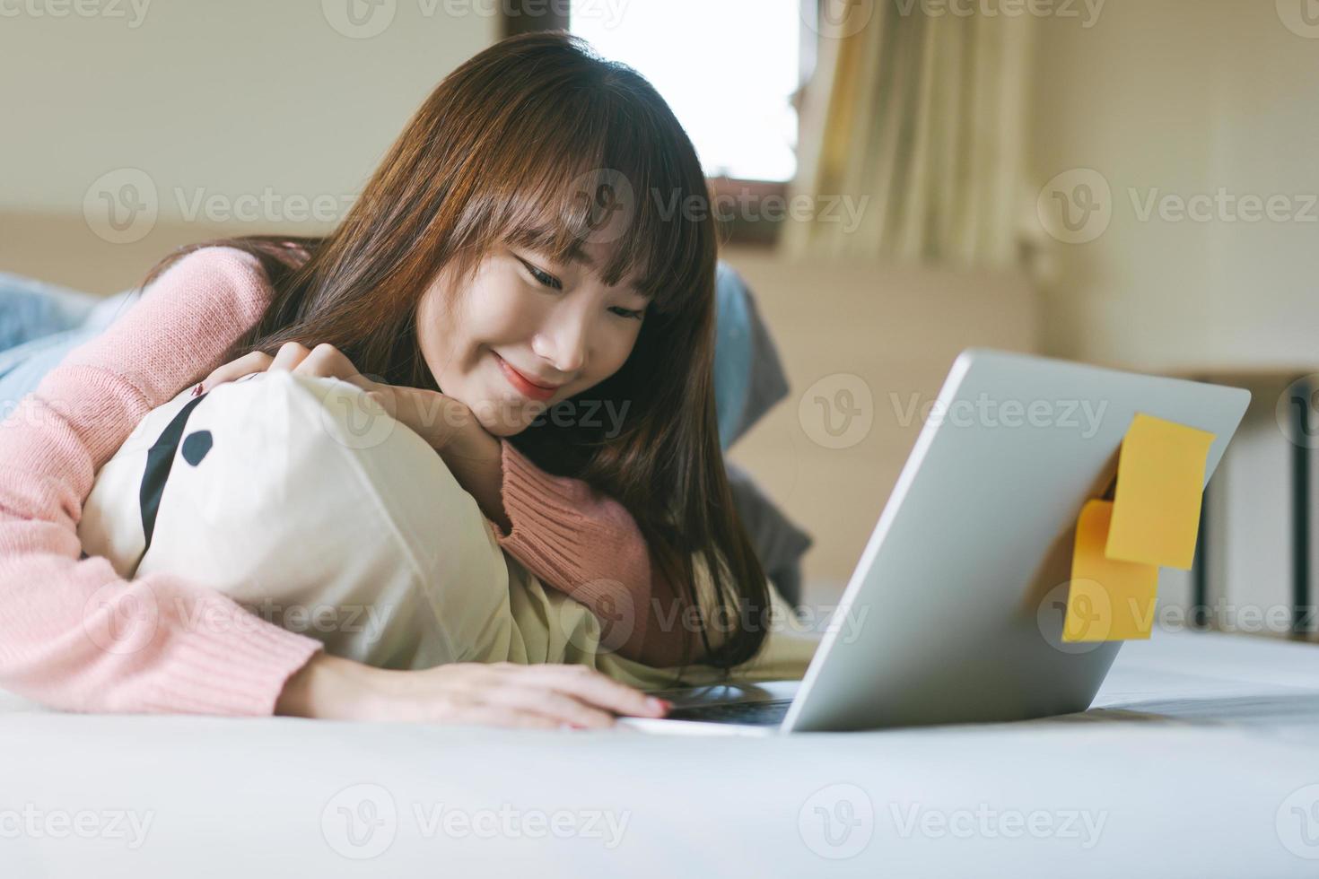 asiatisk tonåringskvinna i sovrummet och använder datorn för arbete och studier på morgonen på helgen. foto