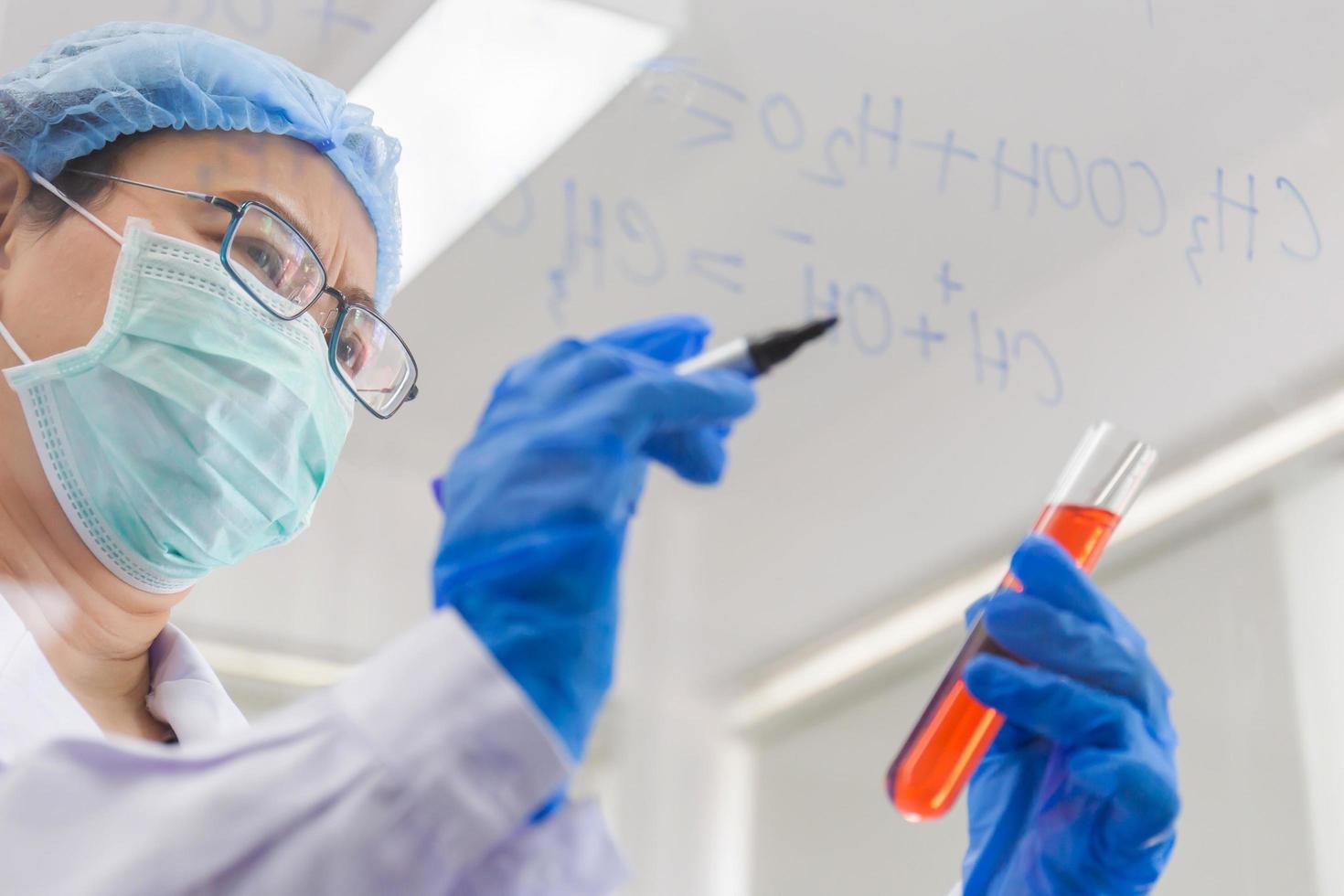 en asiatisk kvinnlig forskare skriver ner formeln för att beräkna kemi på klart glas i ett labb. foto