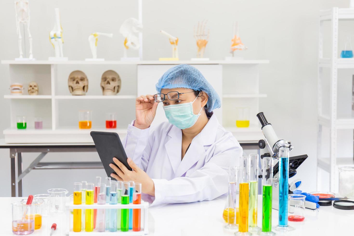 en asiatisk kvinnlig forskare forskar om en kemisk formel i ett labb i en handhållen surfplatta. foto
