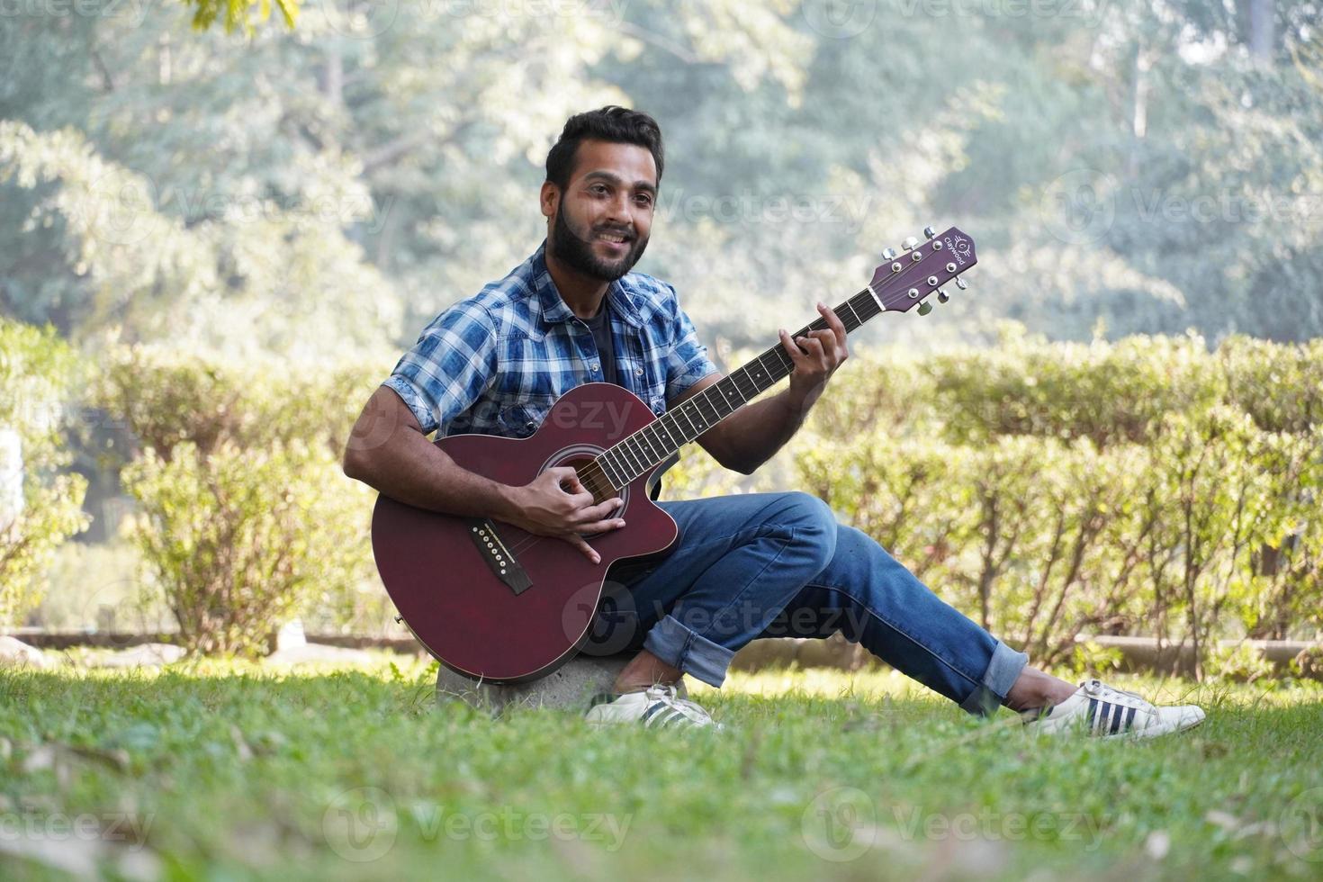 ung pojke med sin gitarr och spelar gitarr i parken foto