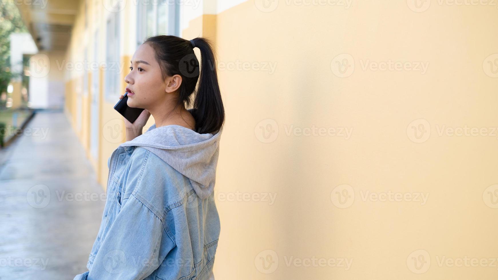 ung flicka pratar på moobile står i skolan, asiatisk flicka. foto